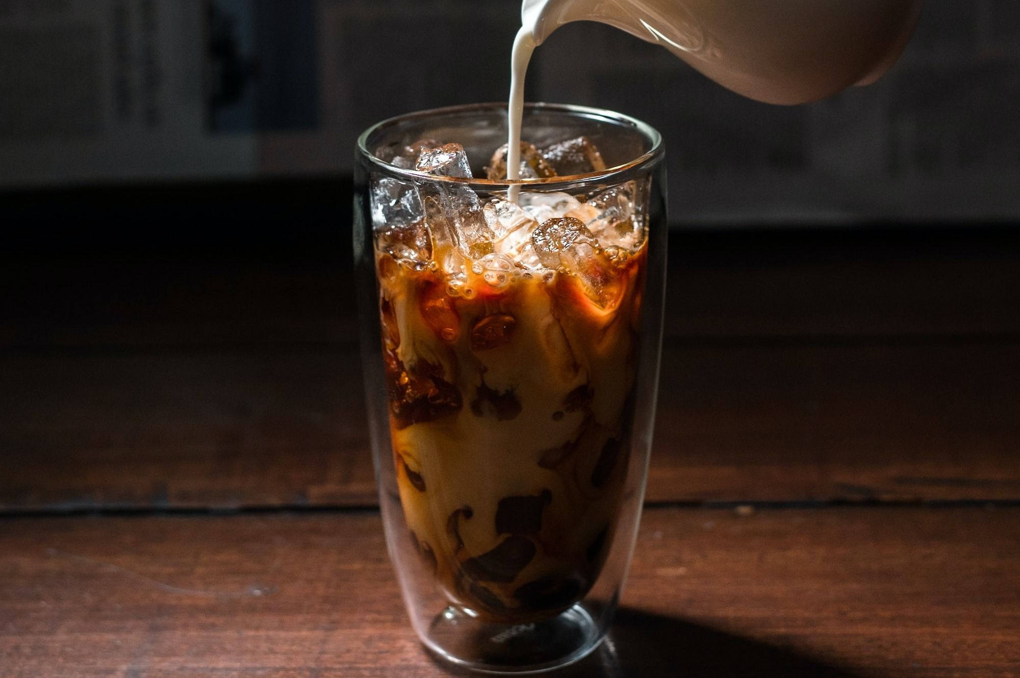 person pouring milk on clear drinking glass